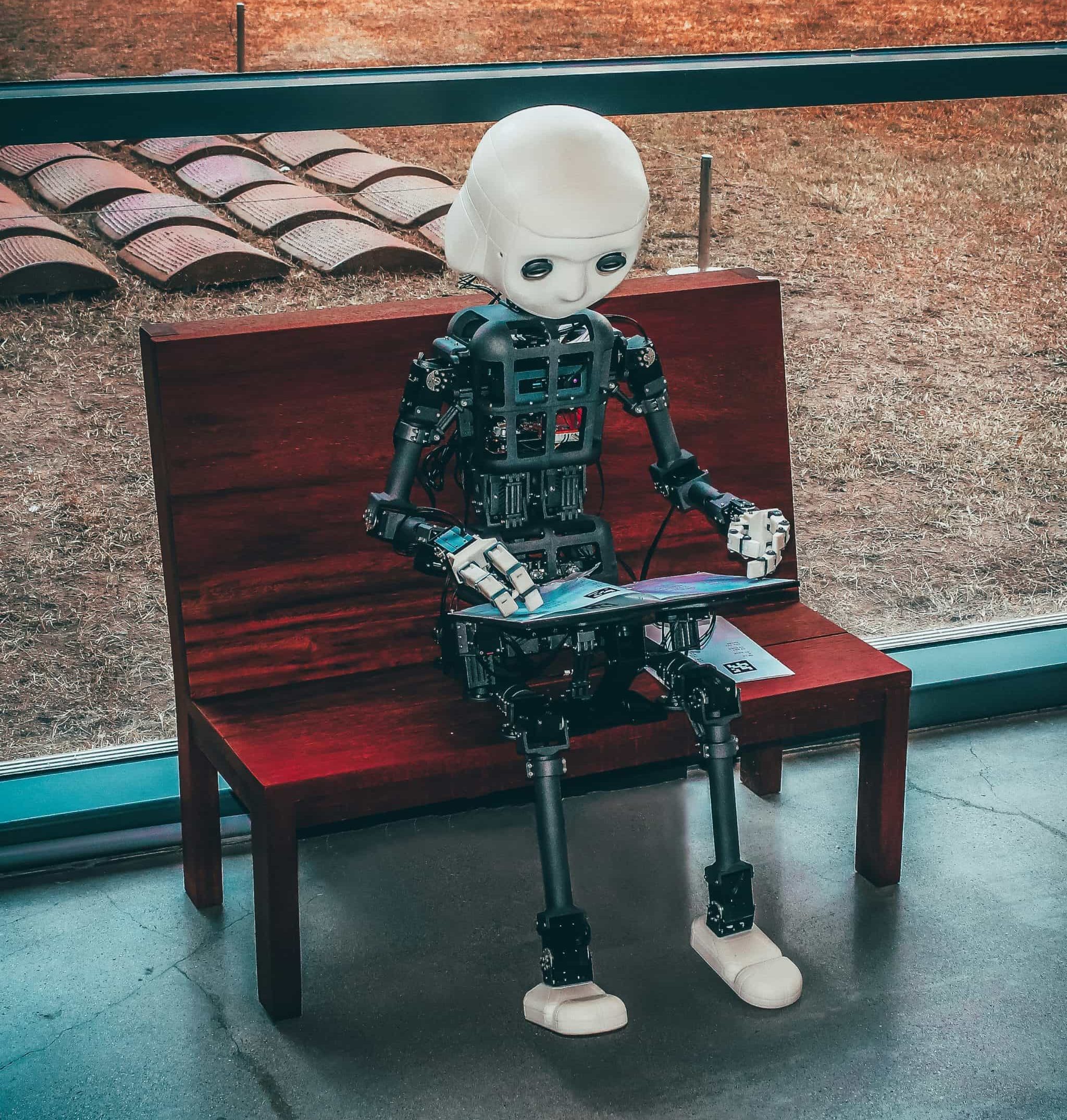Mechanical nuts and bolts robot is sat at a bench with a laptop clearly automating their social media using Quuu