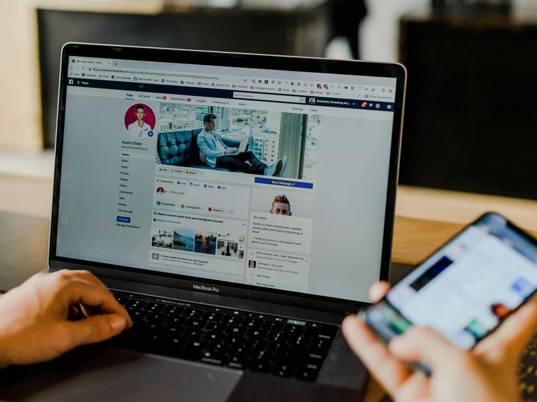 Man looks at laptop screen with Facebook page open, and holds his phone in his right hand with another Facebook page open on that too.